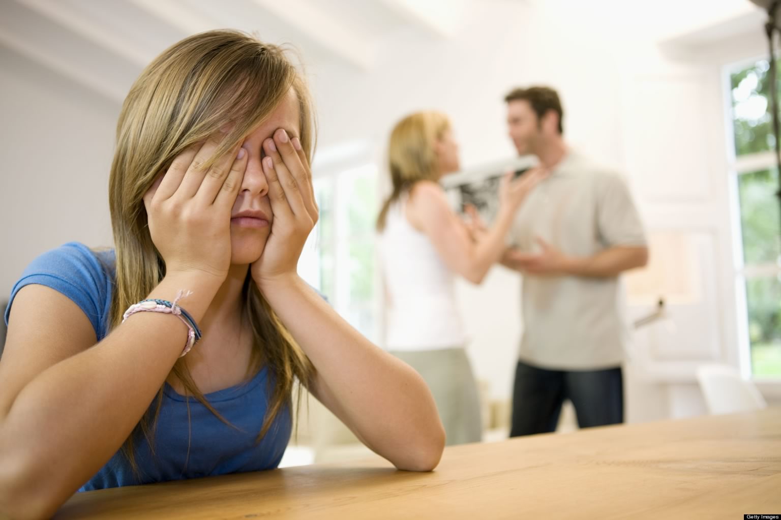 Girl with hands over face while parents argue in background