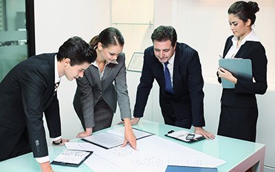People in suits standing around table with documents on it