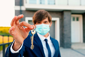 Man wearing face mask holding up key with house in the background