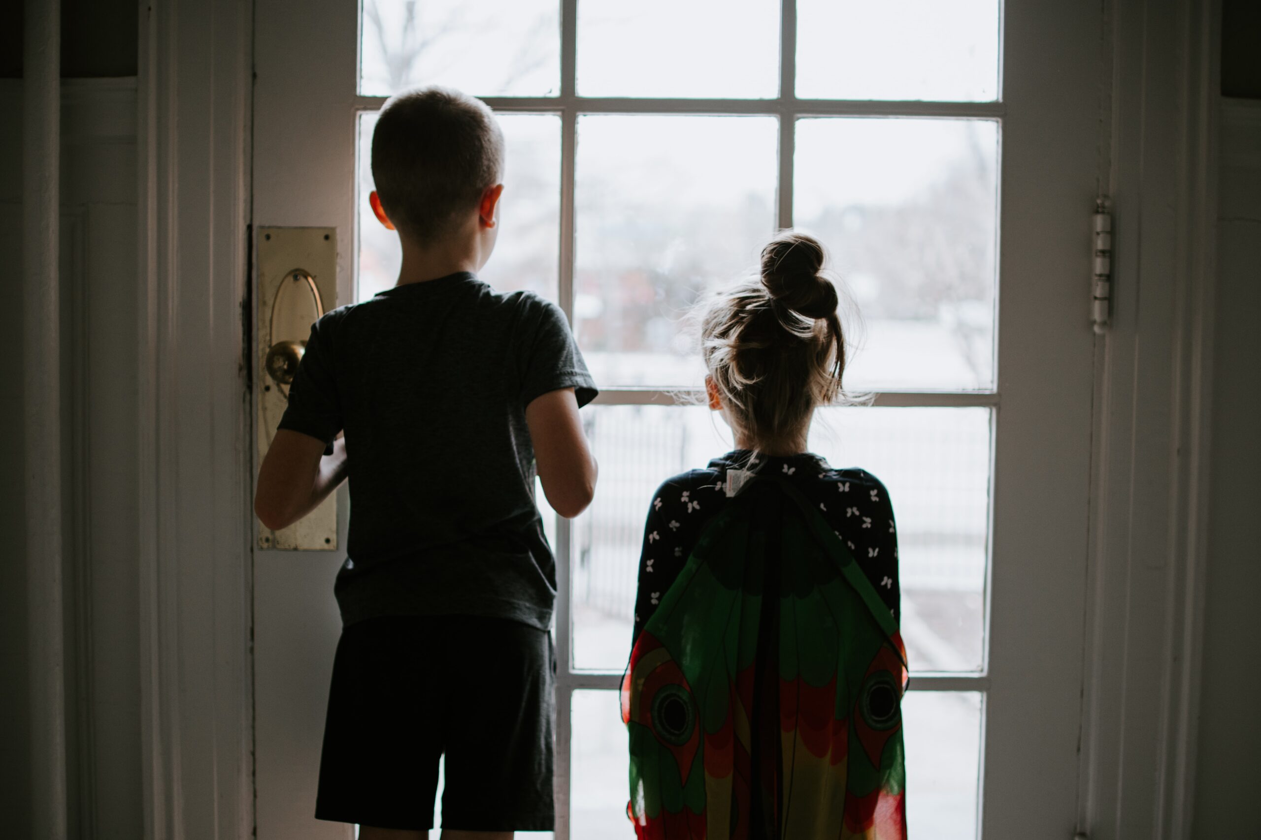 Girl and boy looking out glass door