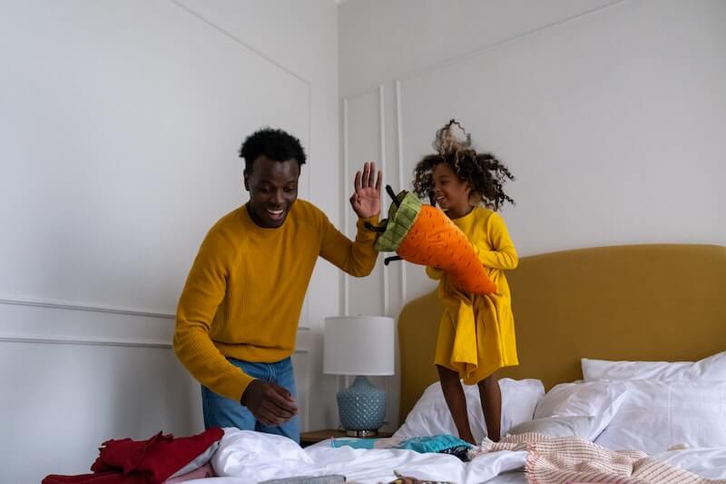 Girl jumping on bed with father next to her