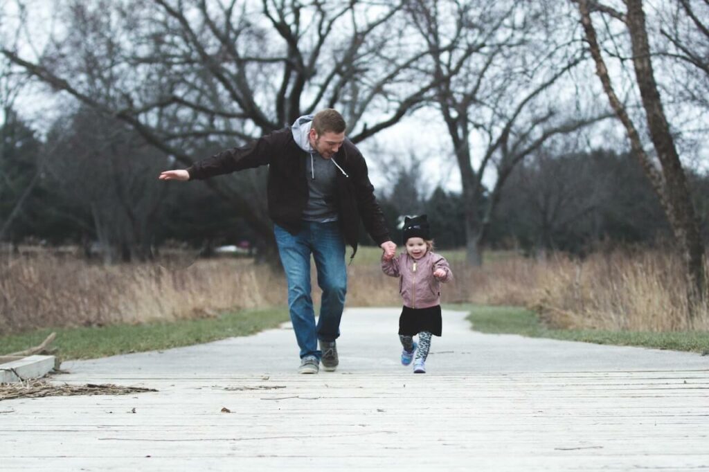 A father joyfully playing with his young child on a wooden path in a park, illustrating the importance of nurturing relationships in parenting coordination.