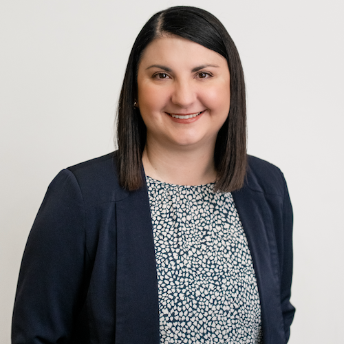 Alyssa, a family lawyer from Rafton Family Lawyers in Sydney, smiling confidently, wearing a navy blazer and patterned blouse against a neutral background, representing the compassionate and expert legal services offered.