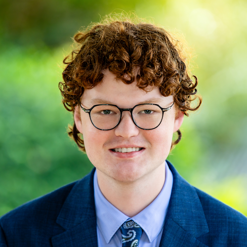 Portrait of a young man with curly hair and glasses, dressed in a blue suit, representing Rafton Family Lawyers in Sydney, providing expert legal services in family law.